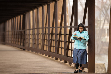Hispanic Woman Reading Bible On A Bridge