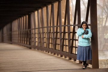 Hispanic Woman Praying And Holding Bible On A Bridge