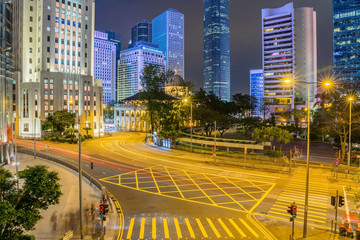 Obraz premium Street traffic in Hong Kong at night. Office skyscraper buildings and busy traffic on highway road with blurred cars light trails. Hong Kong, China