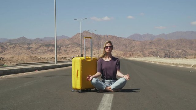 Portrait of young female traveler meditate on hihgway with yellow luggage 4k
