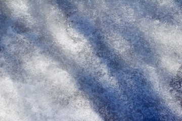 Close up macro view of melting snow on a ground surface with shadows