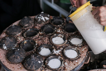 Old woman cooking Vietnamese Street Food in Dalat city market - Banh can on the warm ember stove kitchen 