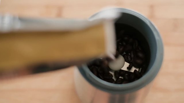 Top view of man barista preparing coffee using steele grinder, beans falling into grinder, 4K UHD