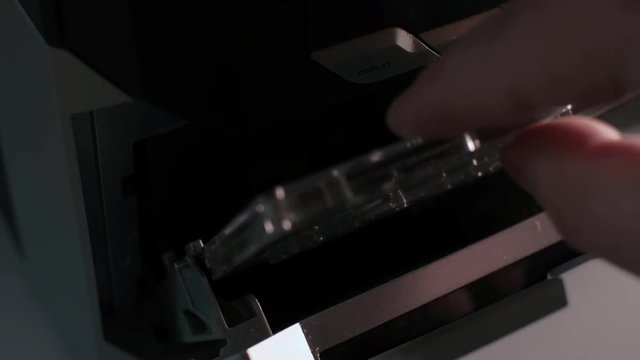 Side close up detail shot, man dj remove cassette in old vintage analogue tape recorder or hifi stereo, dark low light contrast scene, 4H UHD