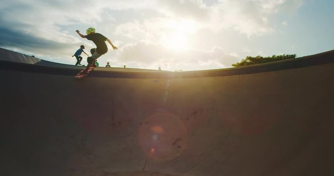 Young skateboarder kid grinding the coping in a pool bowl at sunset, extreme skateboarder kid in skatepark, slow motion