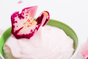 cosmetic cream with pink flower petals, white wood table