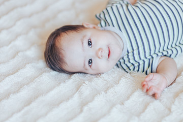 Happy baby lying on white sheet and holding her legs. Playful baby lying down in bed