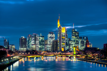Obraz premium Die Skyline der Frankfurter Innenstadt mit Hochhauskulisse am Abend vom Fluß Main aus gesehen