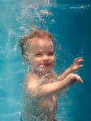 Obraz na płótnie Canvas Cute smiling adorable baby girl diving underwater blue pool. Active lifestyle, child swimming lesson. Water sports activity during family summer vacation in tropical resort