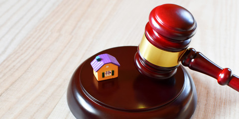 Judges gavel on sound block next to yellow colorful house model on light wooden background with copy space, closeup view. Concept of real estate auction or legal system and law.