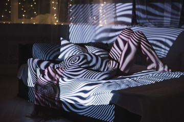 The girl is lying on the bed in the rays of the projector. Abstract portrait of woman in projector...