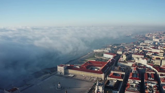 Aerial view; drone flight over Lisbon cityscape; panorama of Portuguese capital with main Commerce Square, Tagus river; morning fog; sunbeams shining and illuminated popular touristic routes of Lisboa