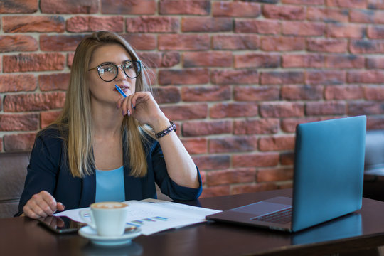 Young business woman sitting at table and taking notes in notebook.On table is laptop, smartphone and cup of coffee.