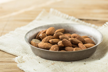  whole almonds in bowl spilled over a rustic wooden table.