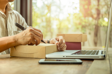 Startup business man writing customer address on parcel with laptop and cell phone on table.