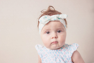 Portrait of eight month girl in the dress with headband, indoors, blurred background