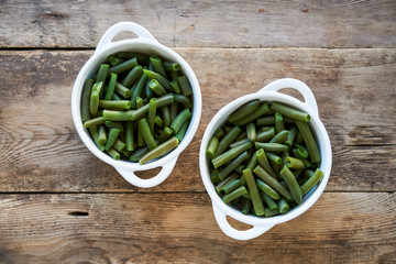 Boiled green beans in white bowls on wooden background