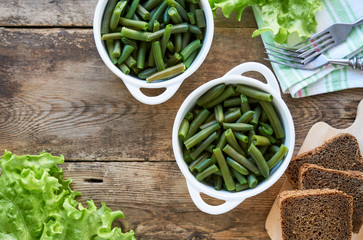 Boiled green beans in white bowls on wooden background