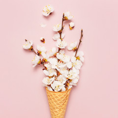 Fototapeta premium Waffle cone with bouquet of spring blooming branches of white flowers on pastel pink background. Creative spring minimal concept. Flat lay top view copy space.