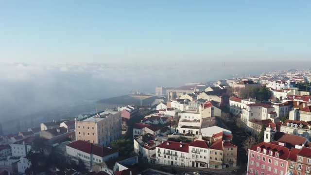 Aerial view; drone flight forward to the ancient building with brown rooftops; foggy time in Lisbon; beautiful winter morning in Portuguese capital; Alfama oldest historic district; view from above