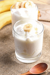 Two glasses of fat homemade yogurt with banana slices on burlap napkin.
