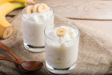 Obraz na płótnie Canvas Two glasses of yogurt with banana slices on burlap napkin. 