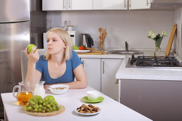 young woman eating healthy food in the kitchen at the table. disappointment in healthy eating tired to eat right, tired of dieting. young woman eating healthy food in the kitchen at the table. 