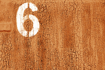 Number 6 in stencil on rusty metal wall in orange tone.