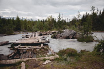 Fototapeta na wymiar Old, broken, wooden bridge over the river in the Altai mountains. Extreme crossing the river