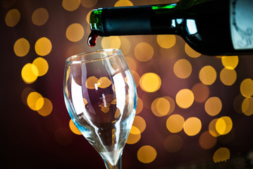  Pouring red wine into the glass. Golden bokeh background.