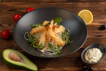 Tempura shrimps with tartar sauce on a black plate on a wooden background