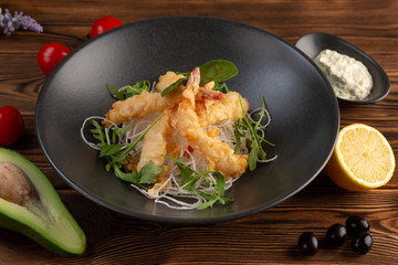 Tempura shrimps with tartar sauce on a black plate on a wooden background