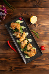 Fototapeta na wymiar Pieces of chicken in batter on a black rectangular plate on a wooden background