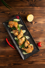 Pieces of chicken in batter on a black rectangular plate on a wooden background