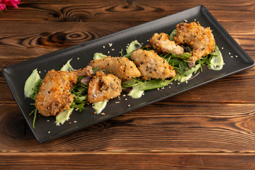 Pieces of chicken in batter on a black rectangular plate on a wooden background