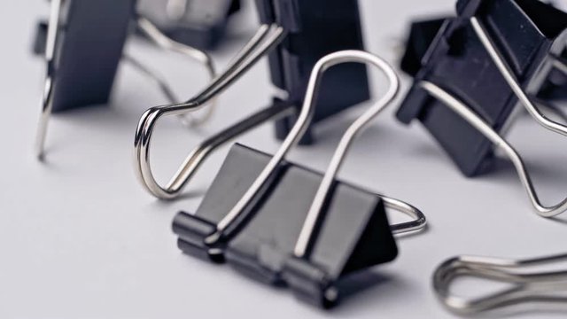 Black paper clips rotate on white background. Office supplies