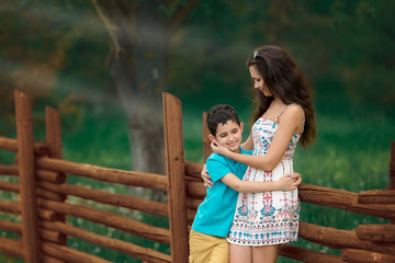 Fototapeta premium Woman and boy are standing near the wooden fence. Mother and son. Summer time. Green background. Mother's day