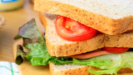 Homemade sandwich breakfast preparing. Close up whole wheat sandwich bread with slice tomatoes and lettuce stacked on wooden cutting board. Cooking ingredient. Food background concept.