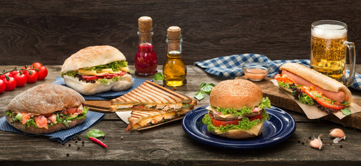 Fototapeta na wymiar Sandwiches and hamburgers, hot dog, beer and tomatoes on the table