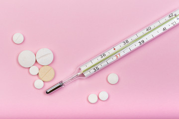 medical  thermometer and white pills on pink  background close up view