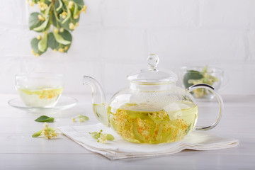 Linden tea in a transparent tea pot.  Glass tea pot with herbal lime tree tea on white background. Medicinal plant, flowers used for herbal teas and tinctures.