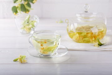 Linden tea in a transparent tea pot.  Glass cup and tea pot with herbal lime tree tea on white background. Medicinal plant, flowers used for herbal teas and tinctures.