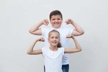 thin happy smiling little girl and thick fat caucasian boy showing biceps muscle on bright...