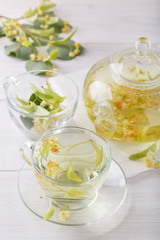Linden tea in a transparent tea pot.  Glass cup and tea pot with herbal lime tree tea on white background. Medicinal plant, flowers used for herbal teas and tinctures.