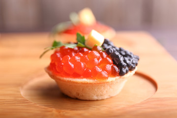 Tasty tartlet with caviar on wooden board, closeup