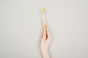 partial view of woman holding bamboo toothbrush on grey background