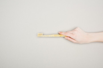 cropped view of woman holding bamboo toothbrush on grey background