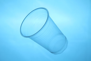 Plastic cup in blue water, plastic pollution of oceans.