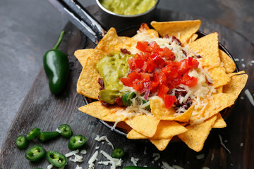 Frying pan with tasty nachos, minced meat, salsa and guacamole on wooden board