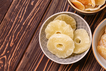 Bowl with tasty dried pineapple on wooden background